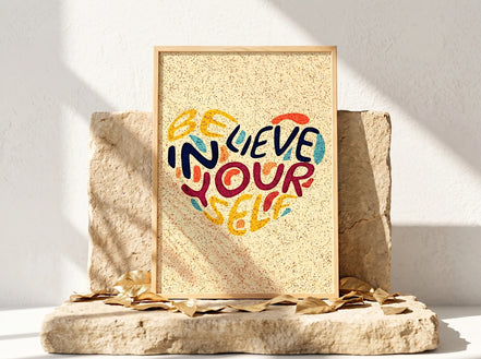 Affiche Essences Agape "Believe in Yourself" en forme de cœur, lettrage coloré sur fond texturé jaune, cadre en bois clair.