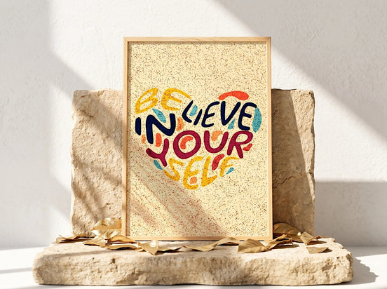 Affiche Essences Agape "Believe in Yourself" en forme de cœur, lettrage coloré sur fond texturé jaune, cadre en bois clair.