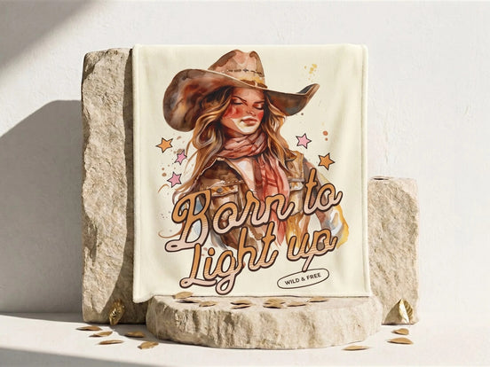 Couverture polaire beige avec illustration d'une cowgirl et l'inscription "Born to Light Up". Essences Agape.