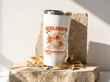 Essences Agape gobelet blanc avec inscription "BELIEVE IN YOURSELF" et motif floral dans des tons orangés et beiges. Idéal pour la motivation et le bien-être.