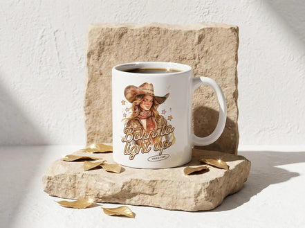 Mug blanc avec illustration d'une cowgirl et l'inscription "Born to light up". Style western, idéal pour le café.
