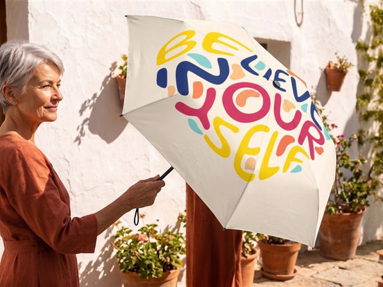 Parapluie pliant Essences Agape blanc avec inscription "Believe Yourself" en lettres multicolores vives. Design inspirant et motivant.