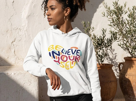 Sweatshirt blanc à capuche Essences Agape avec un cœur multicolore imprimé "Believe in Yourself" en lettres stylisées.