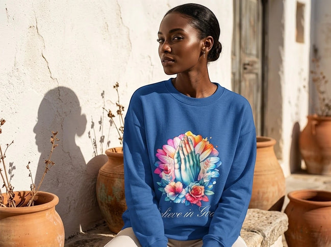 Sweatshirt bleu roi Essences Agape avec un imprimé de mains jointes en prière entourées de fleurs colorées et l'inscription "Believe in God".