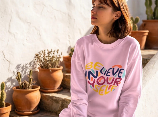 Sweatshirt rose pâle Essences Agape avec inscription "Believe in Yourself" en forme de cœur multicolore. Coupe unisexe.