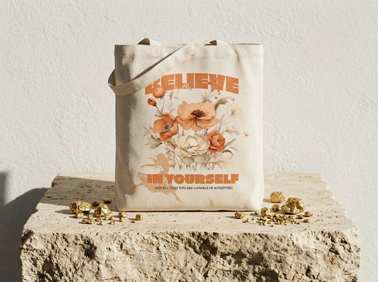 Tote bag en coton écru Essences Agape avec un motif floral abstrait aux tons orangés et un message "Believe in Yourself".