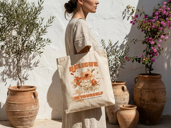 Tote bag en coton écru Essences Agape avec un motif floral aux tons orangés et un message "Believe in Yourself".