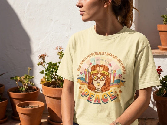 Tee-shirt oversize jaune pâle Essences Agape avec un graphisme rétro d'un visage féminin, citation "Your mind is your greatest weapon – Use it wisely" et le mot PEACE.